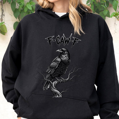May include: A black hooded sweatshirt featuring a graphic print of a raven perched on a bare tree branch. Above the bird, the text F-CAW-F is printed in a stylized, jagged font. The hoodie includes a front kangaroo pocket and long sleeves.
