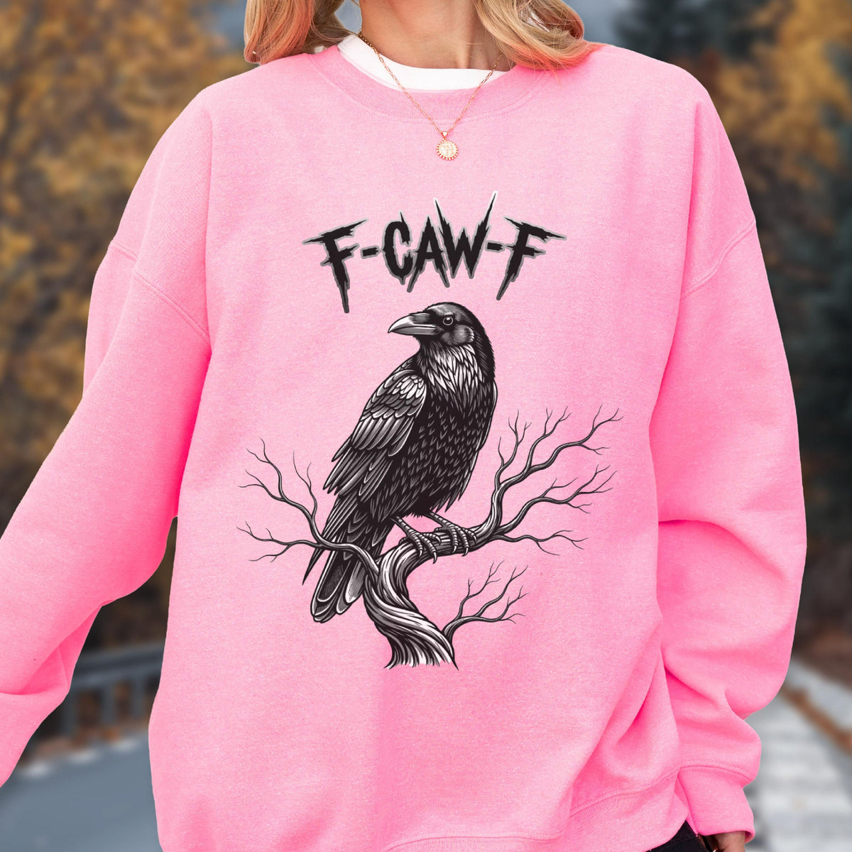 May include: A bright pink long-sleeve sweatshirt featuring a black graphic illustration of a raven perched on a bare tree branch. Above the bird, the text F-CAW-F is printed in a jagged, distressed black font. The garment has a crew neckline.