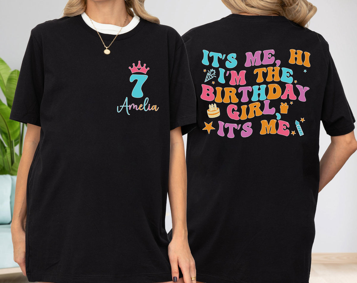 May include: A black short-sleeve t-shirt featuring a front graphic with a pink crown above the number 7 and the name Amelia. The back displays colorful text reading IT'S ME, HI I'M THE BIRTHDAY GIRL IT'S ME, accented with party icons.