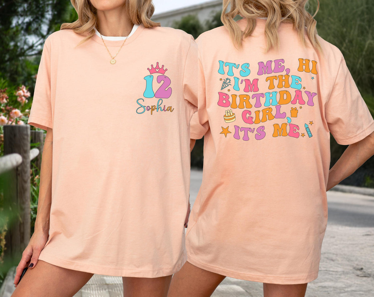 May include: A peach-colored t-shirt featuring a front graphic with the number 12, a crown, and the name Sophia. The back displays the text IT'S ME, HI I'M THE BIRTHDAY GIRL IT'S ME, accompanied by colorful icons of a party hat, cake, and gift.