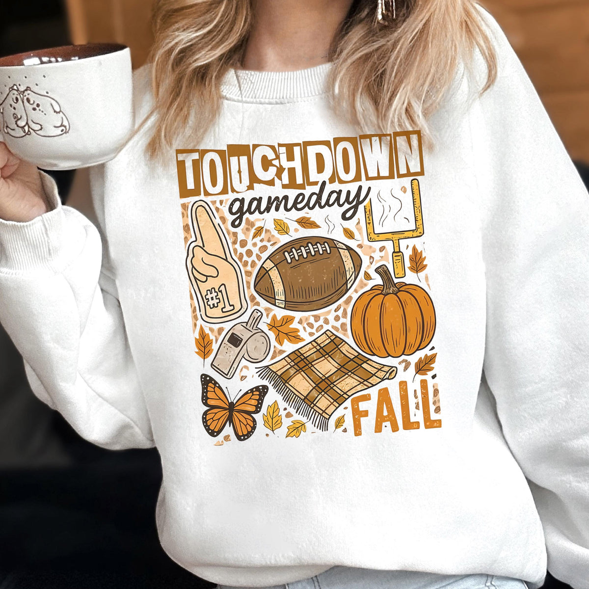 May include: White sweatshirt with a fall-themed graphic. The design includes a football, pumpkin, leaves, and the words "Touchdown Gameday Fall". The sweatshirt has a crew neck and long sleeves.