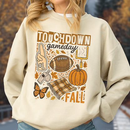 May include: Cream-colored sweatshirt with a fall-themed graphic. The design includes a football, pumpkin, leaves, and the words "Touchdown Gameday Fall". A foam finger, whistle, and butterfly are also featured.