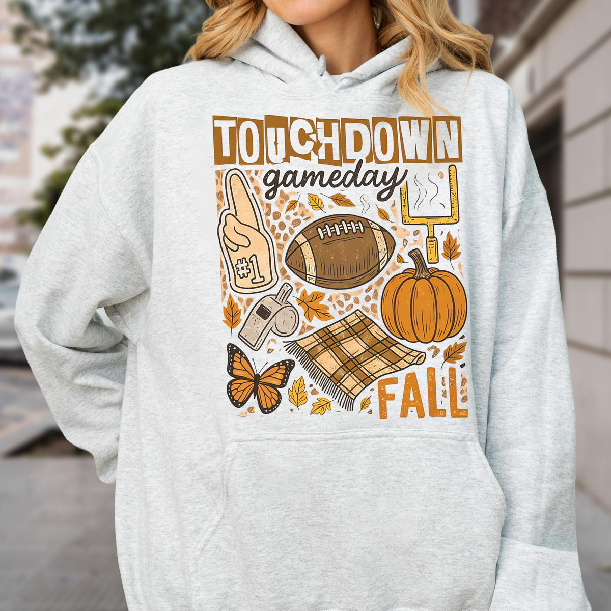 May include: A light gray hoodie with a graphic design featuring the words "TOUCHDOWN gameday FALL". The design includes a football, pumpkin, foam finger, butterfly, and a blanket.