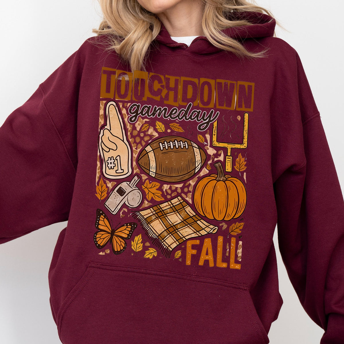 May include: Burgundy hoodie with a fall-themed graphic. The design includes a football, pumpkin, leaves, and the words "TOUCHDOWN gameday FALL!". A foam finger, whistle, and butterfly are also featured.