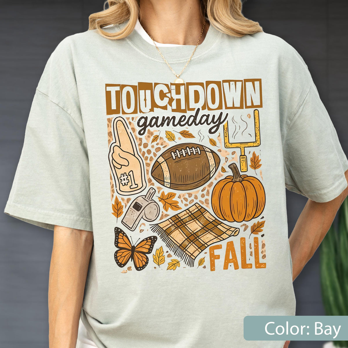 May include: A light green t-shirt with a fall-themed graphic. The design includes a football, pumpkin, leaves, and the words "Touchdown Gameday Fall". A foam finger, whistle, and butterfly are also featured.