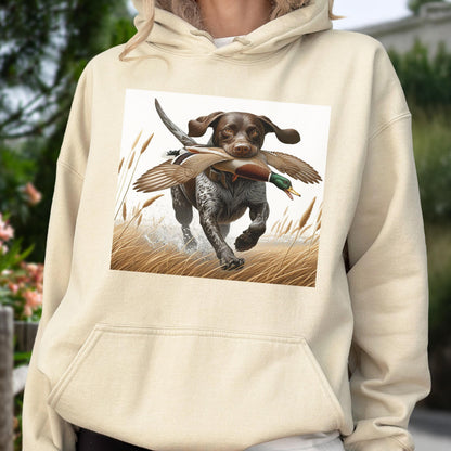May include: A beige hoodie featuring a graphic of a hunting dog with a duck in its mouth, running through tall grass. The dog is brown and white, and the duck has green and brown feathers. The background is a light beige.
