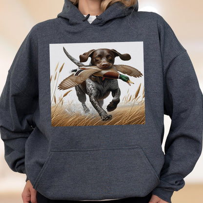May include: Dark gray hoodie featuring a graphic of a hunting dog with a duck in its mouth, running through tall grass. The dog is brown and white, and the duck has brown, white, and green feathers. The background is a light beige.