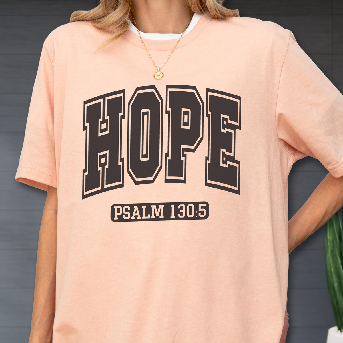 May include: A peach-colored short-sleeve t-shirt featuring the word HOPE in large, bold, dark brown block letters across the chest. Below the word HOPE, the text PSALM 130:5 is printed in a smaller, dark brown rectangular box design.