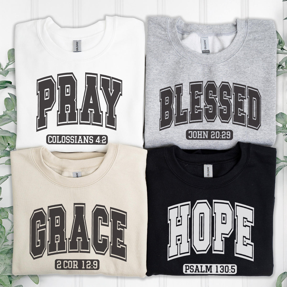 May include: Four crewneck sweatshirts in white, grey, beige, and black. Each features collegiate-style lettering: white with PRAY COLOSSIANS 4:2, grey with BLESSED JOHN 20:29, beige with GRACE 2 COR 12:9, and black with HOPE PSALM 130:5 in bold block font.