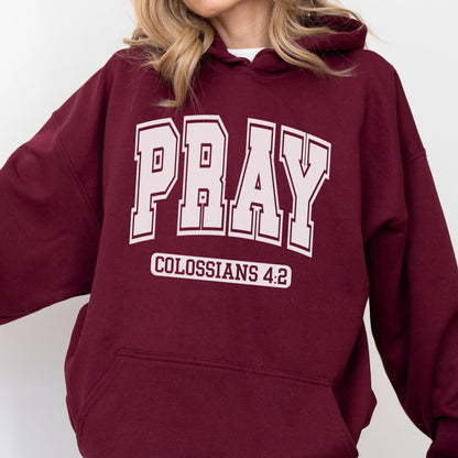 May include: A maroon hooded sweatshirt featuring the word PRAY in large, light pink block letters across the chest. Below the word, the text COLOSSIANS 4:2 is printed in a smaller, light pink font inside a rectangular outline on the front.