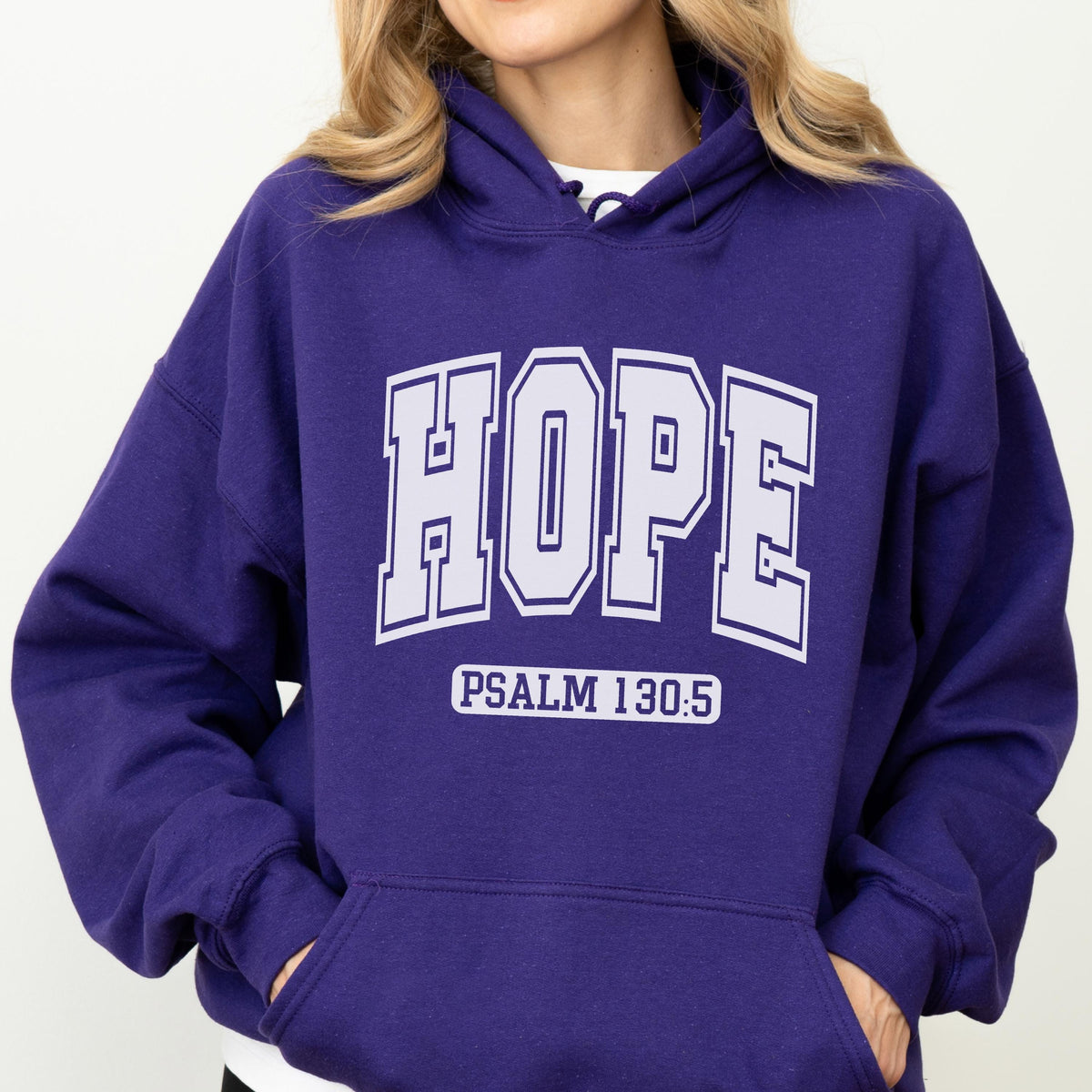 May include: A deep purple hooded sweatshirt featuring the word HOPE in large, white, block-style varsity lettering across the chest. Below the word HOPE, the text PSALM 130:5 is printed in a smaller, white, sans-serif font. The hoodie has a front pocket.
