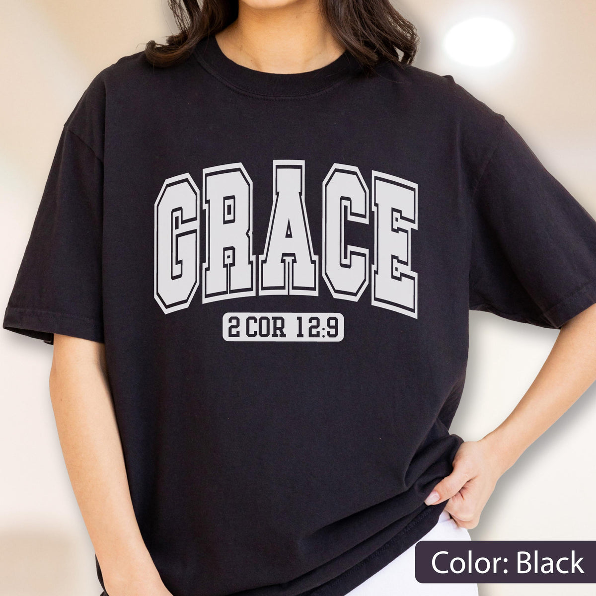 May include: A black short-sleeved t-shirt featuring the word GRACE printed in large, white, block-style varsity lettering across the chest. Below the main text, the scripture reference 2 COR 12:9 is printed in a smaller, white, rectangular box.