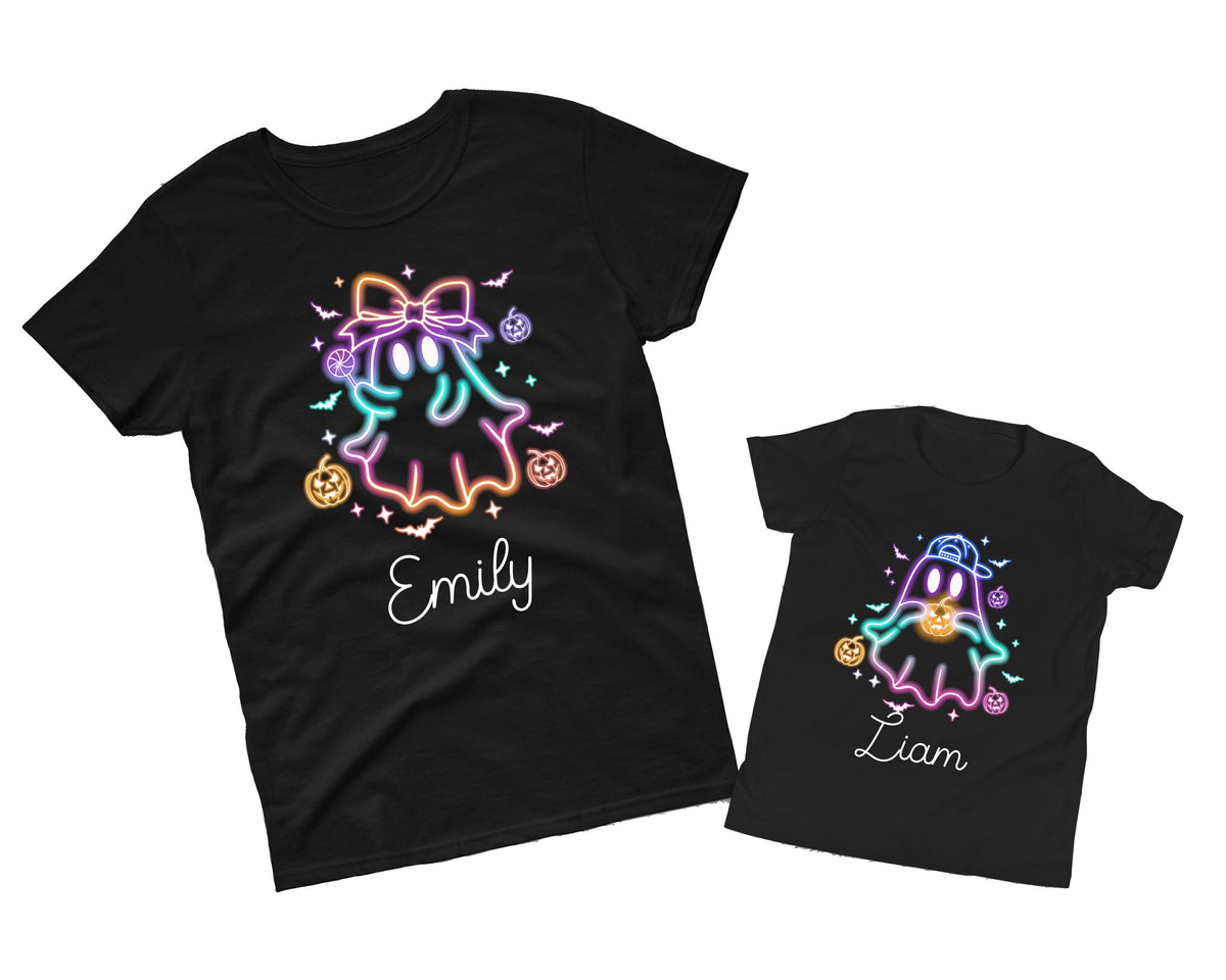 May include: Two black t-shirts with Halloween-themed designs. One shirt features a ghost with a bow, pumpkins, and the name "Emily." The other shirt has a ghost wearing a cap, pumpkins, and the name "Liam." The designs use neon colors.