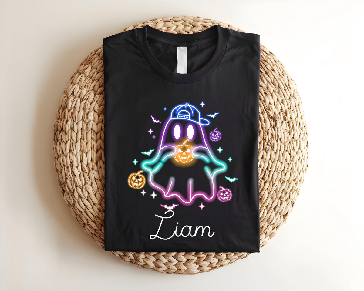 May include: Black t-shirt featuring a neon ghost design wearing a cap and holding a jack-o'-lantern. The design includes bats, stars, and pumpkins. The name "Liam" is written in cursive below the ghost.