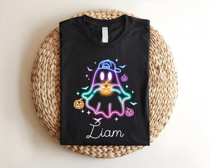 May include: Black t-shirt featuring a neon ghost design wearing a cap and holding a jack-o'-lantern. The design includes bats, stars, and pumpkins. The name "Liam" is written in cursive below the ghost.