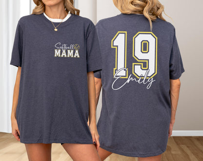 May include: Dark gray t-shirt with white trim. The front features "Softball MAMA" in script and block letters with a softball graphic. The back displays the number "19" in white with a gold outline, and the name "Emily" in script.