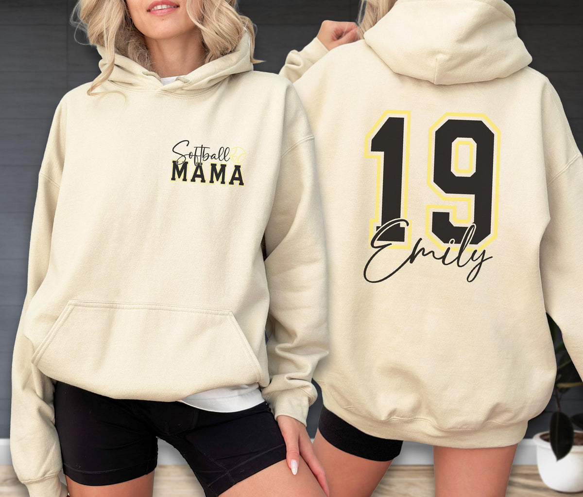 May include: Cream-colored hoodie with a front pocket and hood. The front features the text "Softball MAMA" in black script and yellow lettering. The back displays the number "19" in black with a yellow outline, and the name "Emily" in script.