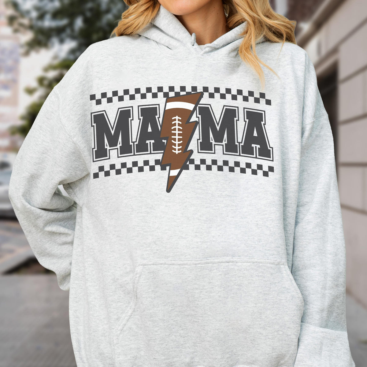 May include: Light gray hoodie with the word "MAMA" in dark gray block letters, a brown football-shaped lightning bolt, and a black and white checkered border. The hoodie has a drawstring hood and a front pocket.