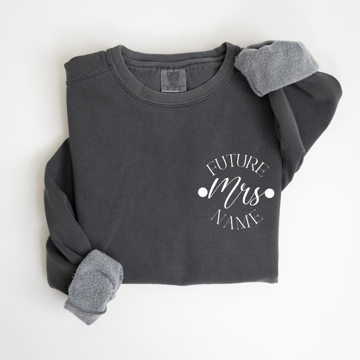 May include: Dark gray sweatshirt with the text "FUTURE Mrs NAME" in white script. The sweatshirt has a crew neck and long sleeves with gray fleece cuffs. The garment is a comfortable, casual style.