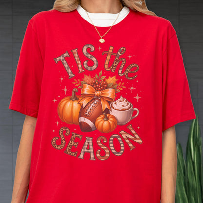 May include: Red t-shirt with a fall-themed graphic. The design includes pumpkins, a football, a cup of whipped cream, and the text "Tis the Season". The text and graphic elements are in various colors and patterns.