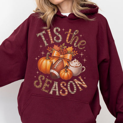 May include: Burgundy hoodie with a fall-themed graphic. The design includes pumpkins, a football, a coffee cup, and the text "TIS the SEASON" in a mix of plaid and leopard print patterns. The graphic is centered on the front of the hoodie.