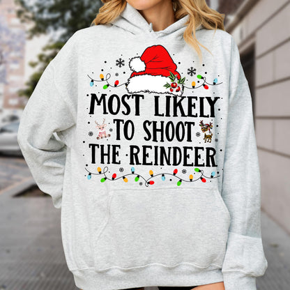 May include: A light gray hooded sweatshirt featuring a red Santa hat graphic at the top, colorful Christmas light strings, and the black text MOST LIKELY TO SHOOT THE REINDEER. Small reindeer illustrations are positioned near the text.
