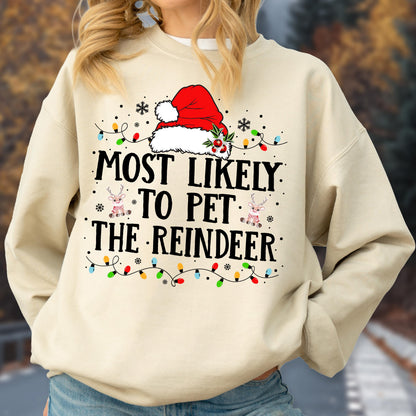 May include: A cream-colored crewneck sweatshirt featuring a graphic of a red Santa hat, colorful Christmas lights, and two small reindeer illustrations. The text reads, "MOST LIKELY TO PET THE REINDEER" in bold black lettering across the chest.