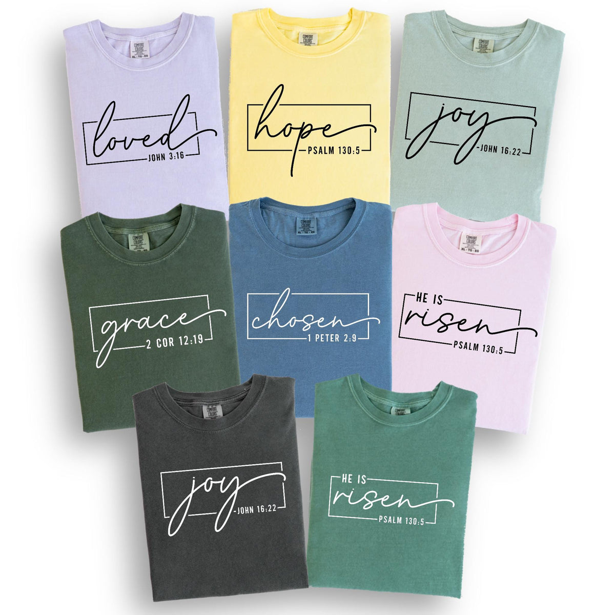 May include: A collection of t-shirts in various colors, including lavender, yellow, and green. Each shirt features a different word in a handwritten font, such as "loved," "hope," and "joy," inside a rectangular frame. The shirts also include Bible verses.
