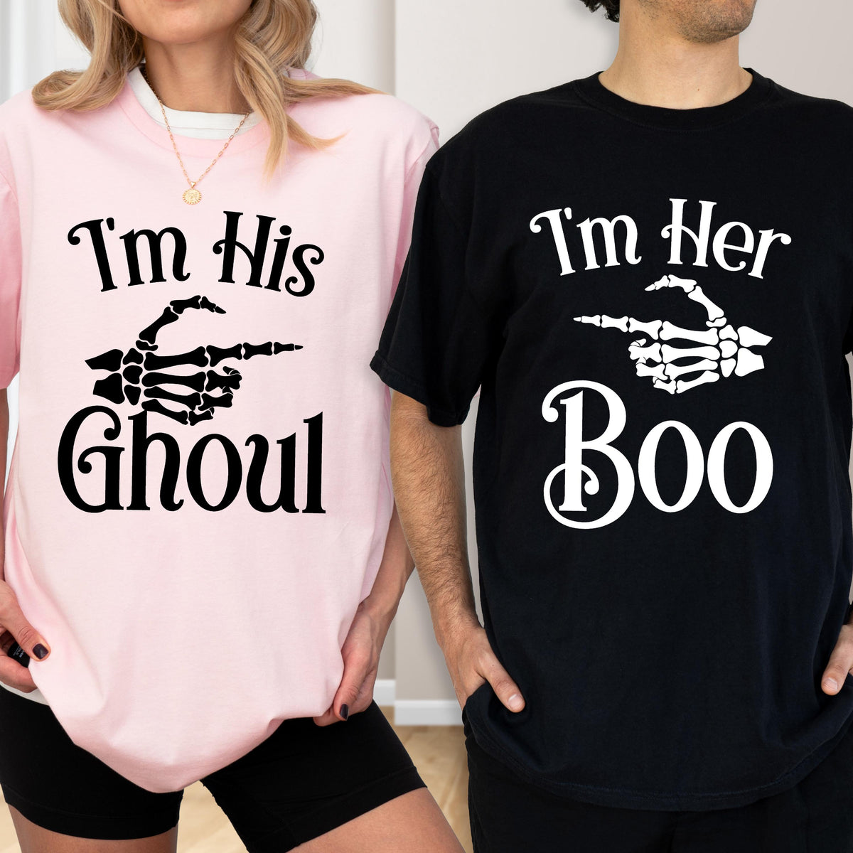 May include: A light pink t-shirt with black text reading I'm His Ghoul and a black skeleton hand graphic, paired with a black t-shirt with white text reading I'm Her Boo and a white skeleton hand graphic pointing toward the other shirt.