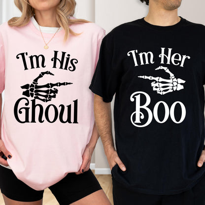 May include: A light pink t-shirt with black text reading I'm His Ghoul and a black skeleton hand graphic, paired with a black t-shirt with white text reading I'm Her Boo and a white skeleton hand graphic pointing toward the other shirt.