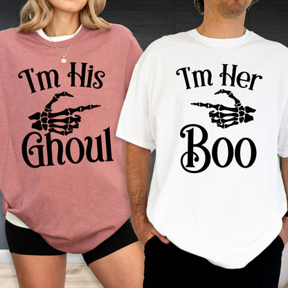 May include: A mauve t-shirt with black text reading I'm His GHOUL and a skeleton hand graphic, paired with a white t-shirt with black text reading I'm Her Boo and a skeleton hand graphic. Both shirts feature short sleeves and crew necklines.