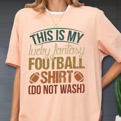 May include: A peach-colored t-shirt featuring the dark green and brown text THIS IS MY lucky fantasy FOOTBALL SHIRT (DO NOT WASH) with two brown football illustrations on the front, worn with a thin gold chain necklace.