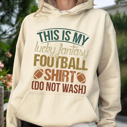 May include: A beige hoodie with the text "THIS IS MY lucky fantasy FOOTBALL SHIRT (DO NOT WASH)" in green, brown, and beige. The design includes two football graphics. The hoodie has a front pocket and a drawstring hood.