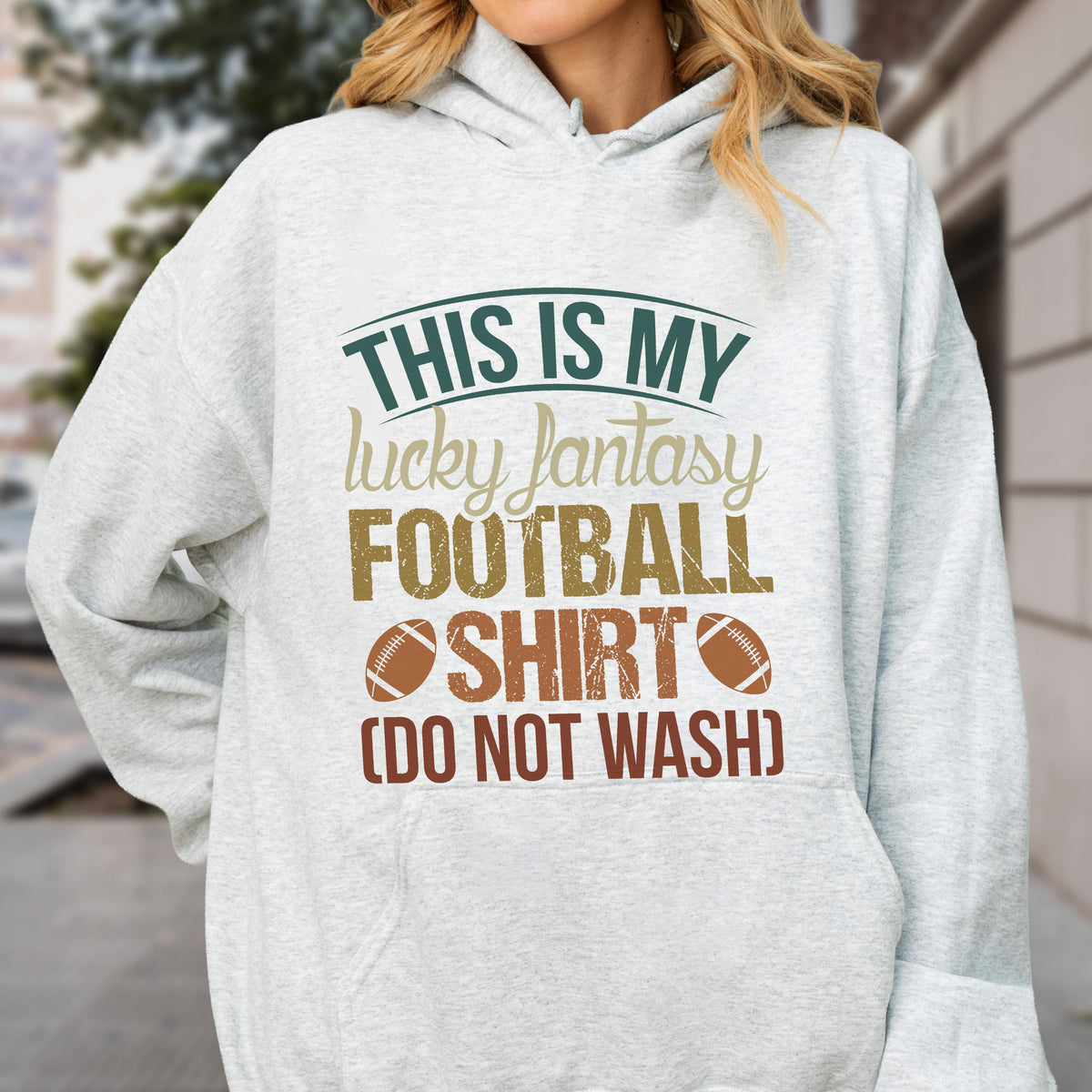 May include: A light gray hoodie with the text "THIS IS MY lucky fantasy FOOTBALL SHIRT (DO NOT WASH)" in green, tan, brown, and white. The design includes two footballs. The hoodie has a drawstring hood and a front pocket.