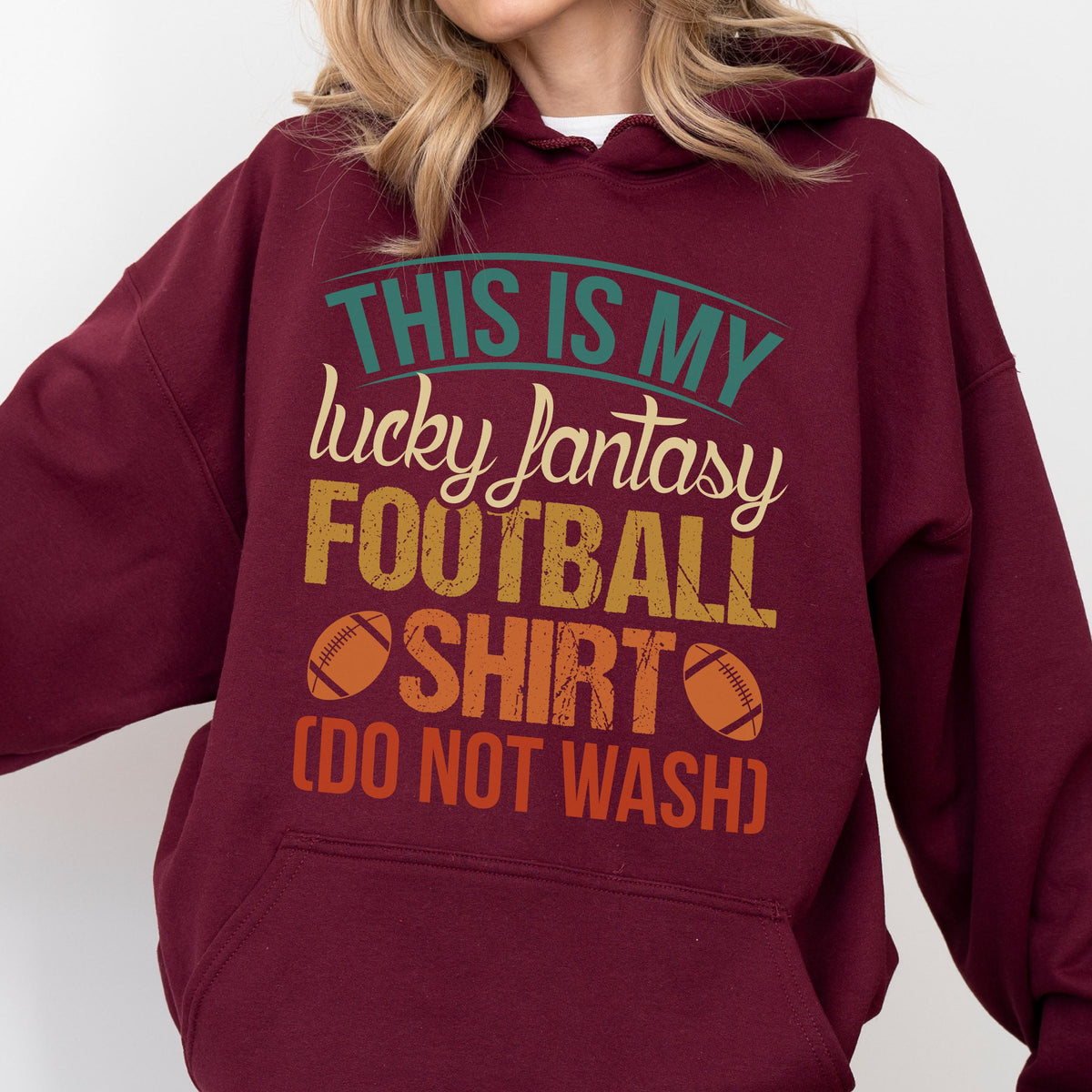 May include: Burgundy hoodie with the text "THIS IS MY lucky fantasy FOOTBALL SHIRT (DO NOT WASH)". The text is in teal, yellow, orange, and white. Two football graphics are on the bottom of the text.