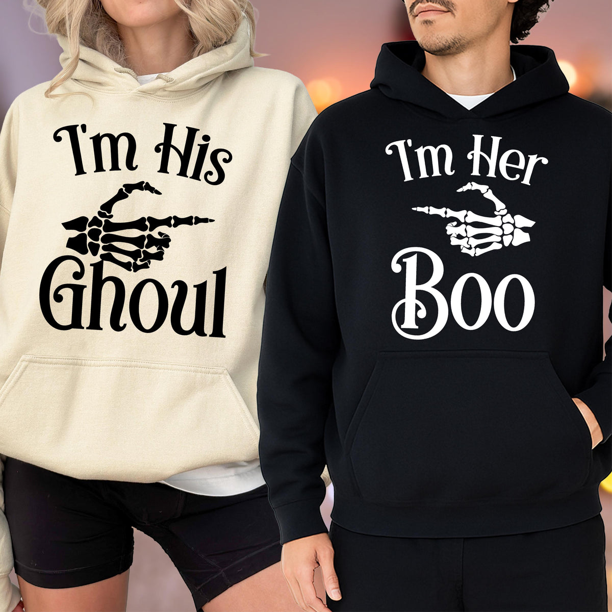 May include: Two hooded sweatshirts, one cream and one black, with Halloween-themed graphics. The cream sweatshirt says "I'm His Ghoul" with a skeleton hand pointing. The black sweatshirt says "I'm Her Boo" with a skeleton hand pointing.