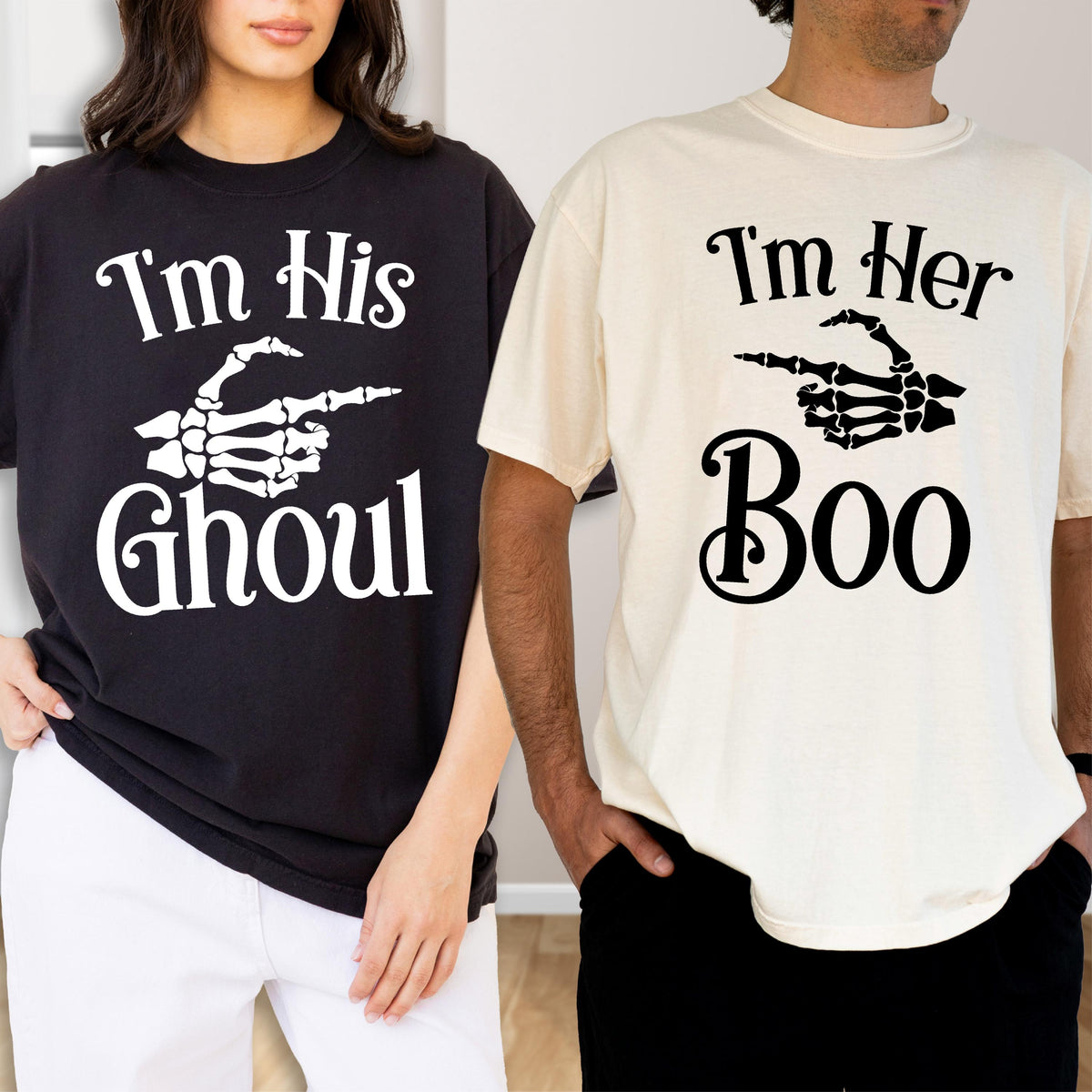 May include: A black t-shirt with white text reading I'm His GHOUL and a white skeleton hand graphic, paired with a cream t-shirt with black text reading I'm Her Boo and a black skeleton hand graphic, both featuring short sleeves and crew necks.