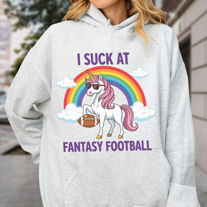 May include: A light gray hooded sweatshirt featuring a graphic of a white unicorn with a pink mane, wearing sunglasses and holding a brown football. Above and below the unicorn, the text reads I SUCK AT FANTASY FOOTBALL, with a rainbow and clouds.
