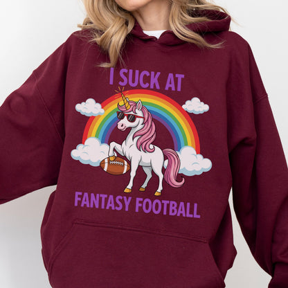 May include: A maroon hooded sweatshirt featuring a graphic of a white unicorn with a pink mane and tail, wearing sunglasses, holding a brown football under a rainbow and clouds. The text reads I SUCK AT FANTASY FOOTBALL in purple capital letters.