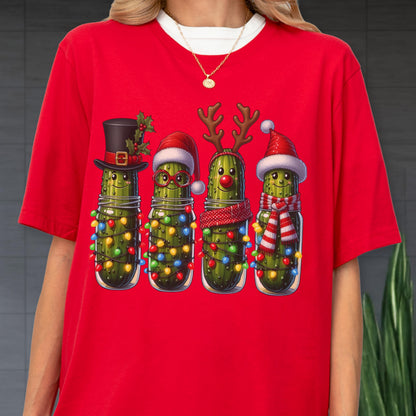 May include: Red t-shirt featuring a festive design of four anthropomorphic pickles in mason jars, each adorned with holiday accessories like a top hat, Santa hat, reindeer antlers, and scarves. The pickles are decorated with colorful Christmas lights.