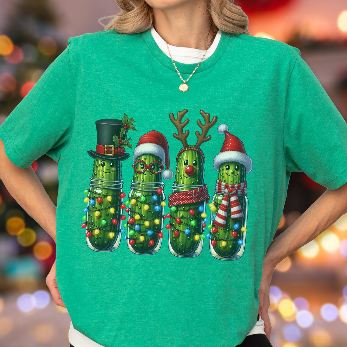 May include: Green t-shirt featuring a festive graphic of four pickles in jars, each adorned with holiday accessories. The pickles are decorated with a top hat, Santa hat, reindeer antlers, and a scarf, all surrounded by colorful string lights.