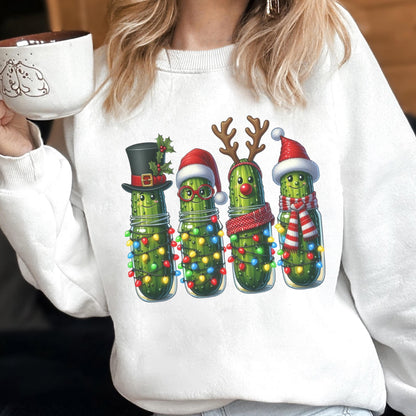 May include: A white crewneck sweatshirt featuring a graphic of four green pickles in glass jars. The pickles are decorated with Christmas elements including a top hat, Santa hats, reindeer antlers, a red nose, a scarf, and colorful string lights.