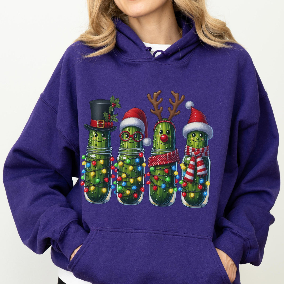 May include: A deep purple hooded sweatshirt featuring a graphic of four green pickles in glass jars. Each pickle is decorated for the holidays with items including a black top hat, a Santa hat, reindeer antlers, and a red and white striped scarf.