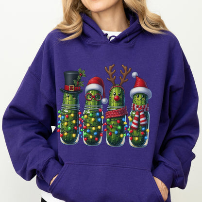 May include: A deep purple hooded sweatshirt featuring a graphic of four green pickles in glass jars. Each pickle is decorated for the holidays with items including a black top hat, a Santa hat, reindeer antlers, and a red and white striped scarf.