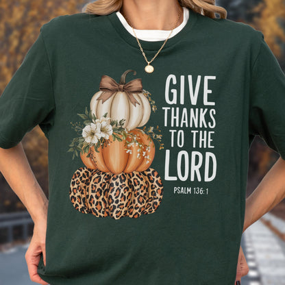 May include: Dark green t-shirt featuring a stacked pumpkin design with a leopard print base, orange and white pumpkins, and floral accents. The text "GIVE THANKS TO THE LORD" is printed in white, with "PSALM 136:1" below.