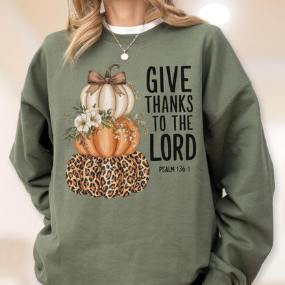 May include: Green sweatshirt featuring a stacked pumpkin design. The top pumpkin is white with a brown bow, the middle pumpkin is orange, and the bottom pumpkin has a leopard print. The text "GIVE THANKS TO THE LORD" is printed in black.