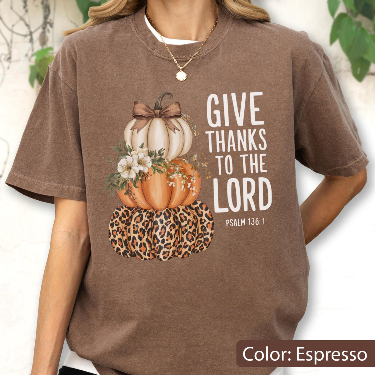 May include: Espresso-colored t-shirt featuring a stacked pumpkin design with a leopard print base, orange and white pumpkins, and floral accents. The text "GIVE THANKS TO THE LORD" is printed in white, with "PSALM 136:1" below.