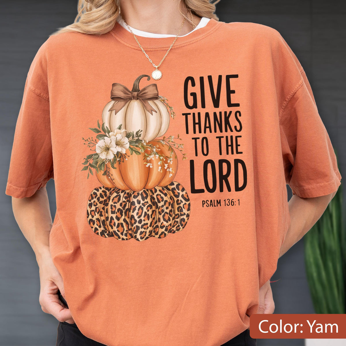 May include: Orange t-shirt with a stacked pumpkin design. The top pumpkin is white with a brown bow, the middle pumpkin is orange, and the bottom pumpkin has a leopard print. The text "GIVE THANKS TO THE LORD" is printed on the right side.
