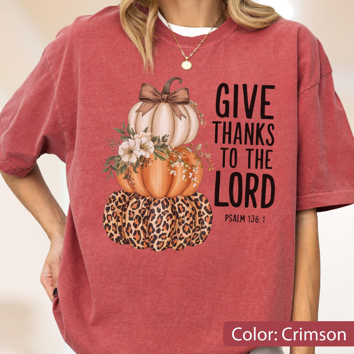 May include: Crimson-colored t-shirt featuring a stacked pumpkin design with a leopard print base, an orange pumpkin, and a cream-colored pumpkin topped with a bow. The text "GIVE THANKS TO THE LORD" is printed on the right side.