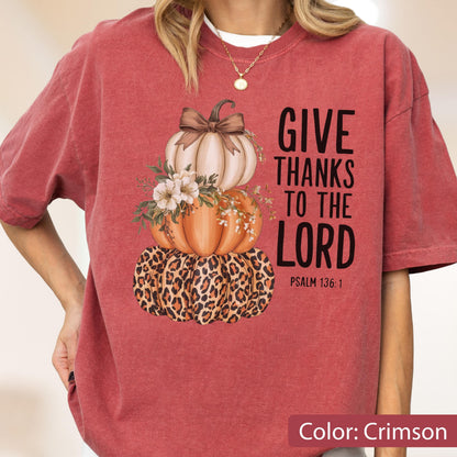May include: Crimson-colored t-shirt featuring a stacked pumpkin design with a leopard print base, an orange pumpkin, and a cream-colored pumpkin topped with a bow. The text "GIVE THANKS TO THE LORD" is printed on the right side.